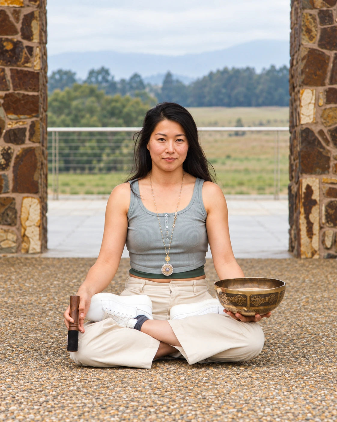 Founder of YamOGA seated outdoors holding a Tibetan singing bowl and mallet